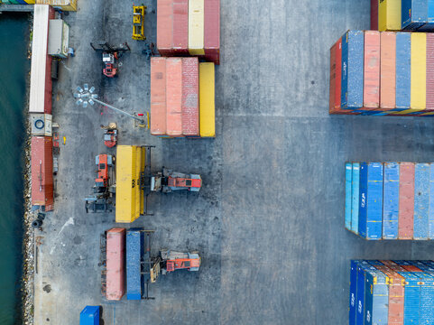 Aerial view of stacked shipping containers casting long shadows on the concrete ground, contrasting with the bright colors of the metal boxes, Figueira da Foz, Coimbra District, Portugal.