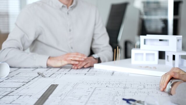 Handshaking between two architects finalizing a construction project deal, business partners agreeing on engineering blueprints and architectural models in an office, close up