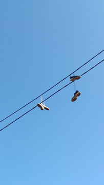 Urban Shoefiti Featuring Sneakers Hanging from an Overhead Power Line Against a Clear Blue Sky