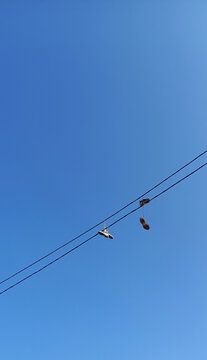 Urban Shoefiti Featuring Sneakers Hanging from an Overhead Power Line Against a Clear Blue Sky