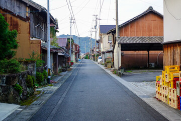 Fototapeta premium Quiet village street with traditional wooden houses in Shikoku Japan leading toward distant mountains under soft light