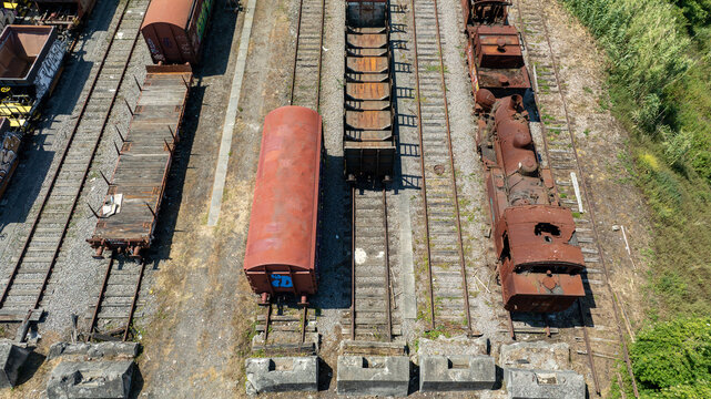 Aerial view of aged, rusty train cars and locomotives sit on parallel tracks, their weathered surfaces a stark contrast to the surrounding muted landscape, Vila Nova de Gaia, Portugal.