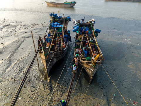 Aerial view of two boats laden with goods and people, connected by a precarious walkway over the muddy banks, Chattogram, Bangladesh.