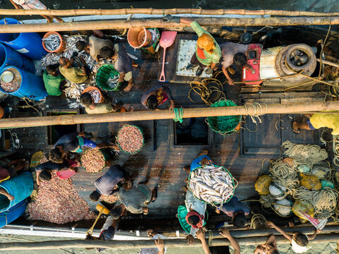 Aerial view of a bustling fishing boat teeming with activity, loaded with the day's catch, creating a vibrant scene on the water, Chattogram, Bangladesh.