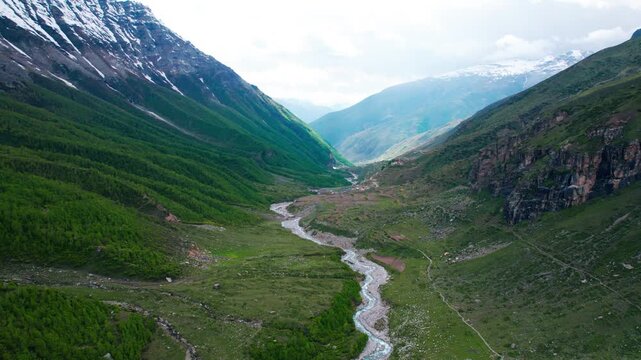 4K Aerial landscape of snowy mountains high above the forest at Sural Bhatori, Pangi Valley, India. Chenab river flowing in green meadows at Chamba district. Nature background. Travel and holidays con
