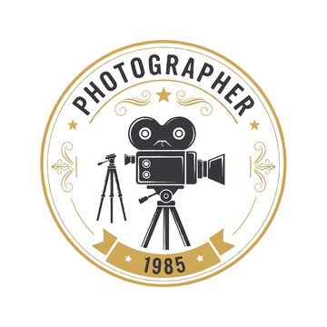 Vintage photographer emblem featuring a classic film camera on a tripod with an ornate circular seal and 1985 banner.