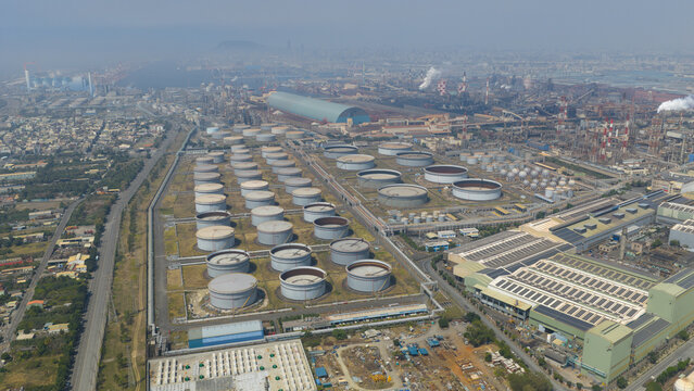 Aerial view of a vast industrial landscape where rows of tanks meet towering structures under a hazy sky, Dalin refinery, Kaohsiung City, Taiwan.