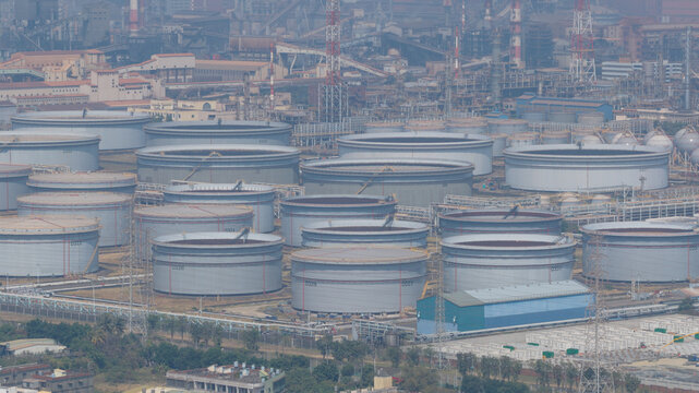 Aerial view of rows of silver storage tanks glint under a hazy sky, juxtaposed against the intricate network of pipes and industrial structures, Kaohsiung City, Taiwan.