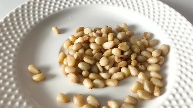 Peeled pine nuts in a white plate close-up. Macro video. pine nut kernel