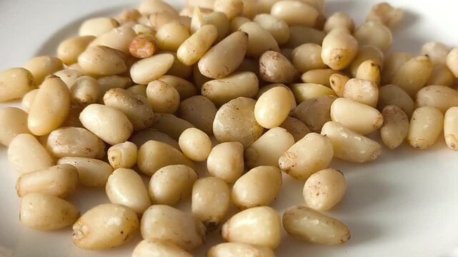 Peeled pine nuts in a white plate close-up. Macro video. pine nut kernel