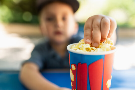 A 5-6-year-old preschooler eats popcorn at a park cafe. Fast food during a summer walk. Children eat street food.