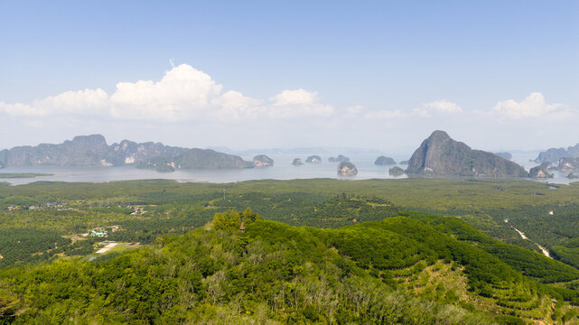 Aerial view of limestone karsts rising from the calm sea surrounded by dense mangrove forests and lush tropical greenery in Phang Nga Bay, Thailand.