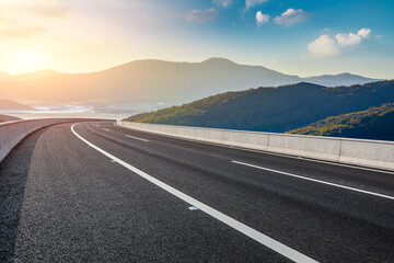 Asphalt highway through mountain landscape under sunset sky