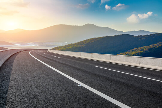 Asphalt highway through mountain landscape under sunset sky