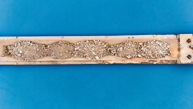 Aerial view of a stark contrast between the azure water and the rugged texture of the piles of rocks on the pier, Sremska Mitrovica, Vojvodina, Serbia.