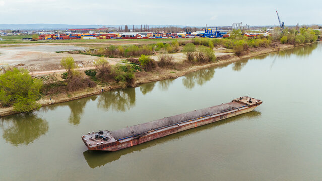 Aerial view of a long barge sails on the tranquil river, reflecting the sky and nearby industrial landscape, Sremska Mitrovica, Vojvodina, Serbia.
