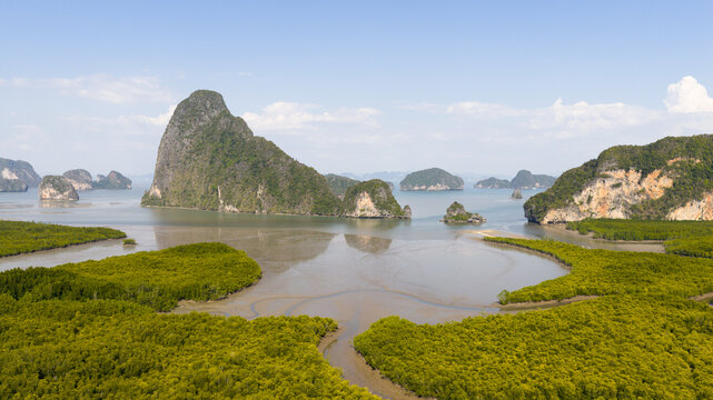 Aerial view of limestone karst islands rising from the sea surrounded by lush green mangrove forests under a clear blue sky Phang Nga, Thailand.