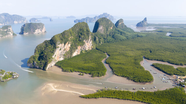 Aerial view of limestone cliffs and lush mangrove forests along a winding river with small boats in Phang Nga Bay, Phang Nga, Thailand.