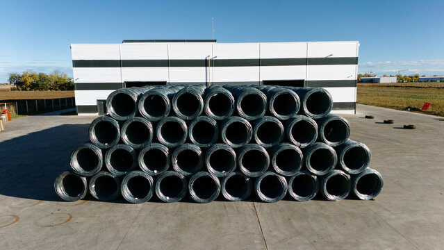 Aerial view of stacked metal coils gleaming under the sun against a modern building's monochrome facade, Sremska Mitrovica, Vojvodina, Serbia.