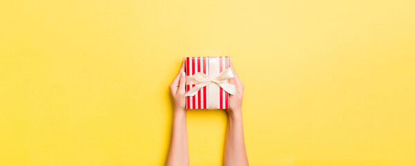 Woman arms holding gift box with colored ribbon on yellow table background, top view and copy space for you design © sosiukin