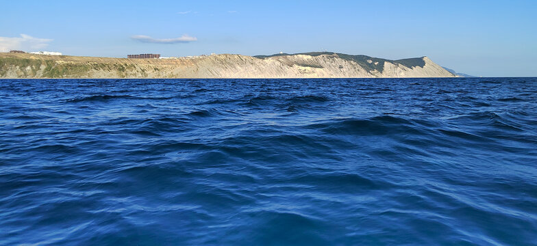 View from the water of the majestic limestone cliffs of Punta Galea in the Bay of Biscay. Deep blue sea with light ripples under a clear sky. Atmosphere of sea travel and coastal beauty in Spain.