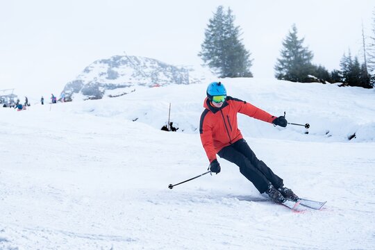 View of a skier in a vibrant red jacket carving through the pristine, powdery snow on a mountain slope, contrasted against the soft, overcast sky, Val-d Illiez, Valais, Switzerland.