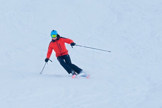 View of a skier in vibrant red jacket and blue helmet carves through pristine white snow, a dance of color and motion on the slopes, Val-d Illiez, Valais, Switzerland.