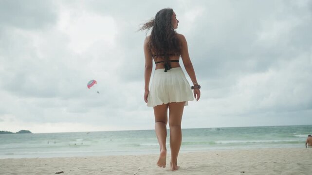 Ladies watch windfilled ocean display. Female figures gaze at turbulent waters and breezy skies attentively. Women stand on coastlines witnessing gusty waves and flying kites passionately