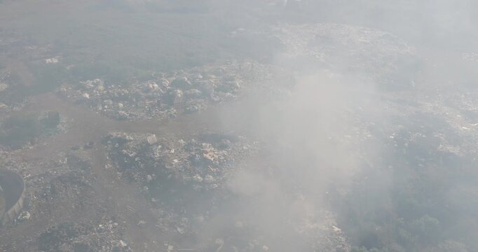 Aerial panning view. Burning rubbish causing greenhouse gas, contributor to climate change.  Extreme Poverty. People living alongside dumpsite struggling to survive through waste picking.