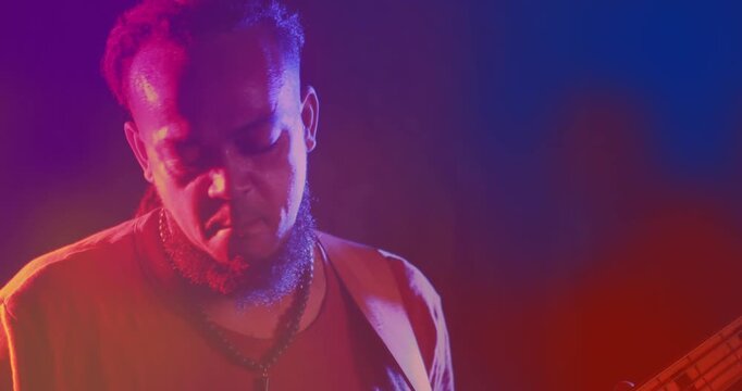 Animation of red and blue light blurs over african american man with dreadlocks playing bass guitar