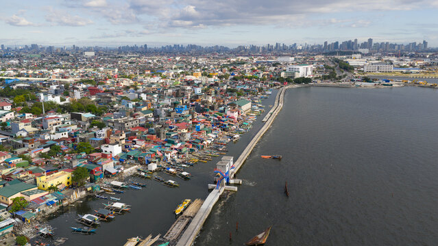 Aerial view of the dense coastal residential area and seawall with fishing boats along the shore in Navotas, Metro Manila, Philippines.