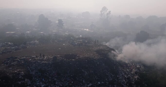 Aerial close-up panning view. Burning rubbish causing greenhouse gas, contributor to climate change.  Extreme Poverty. People living alongside dumpsite struggling to survive through waste picking.
