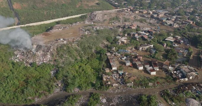 Aerial panning view. Burning rubbish causing greenhouse gas, contributor to climate change.  Extreme Poverty. People living alongside dumpsite struggling to survive through waste picking.