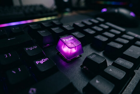 Close up of purple illuminated pause button on black computer keyboard with vibrant RGB lighting edge detail