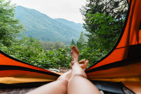 Bare feet resting inside an orange tent with a beautiful view of green mountain peaks.