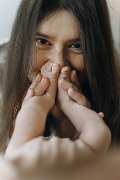 Happy Mothers day! Mother kissing newborn baby feet in bedroom. Love and family concept. Mom holding sweet little infant legs, close up. Adoption and maternity. Child health and care