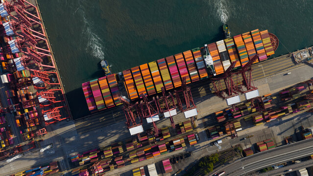 Aerial view of Kwai Tsing Container Terminal V with a large cargo ship, red gantry cranes, and colorful stacked containers in Hong Kong, New Territories, Hong Kong.