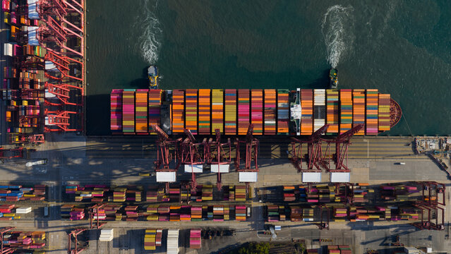 Aerial view of Kwai Tsing Container Terminal V with a large cargo ship being loaded by red gantry cranes and tugboats in Hong Kong, New Territories, Hong Kong.