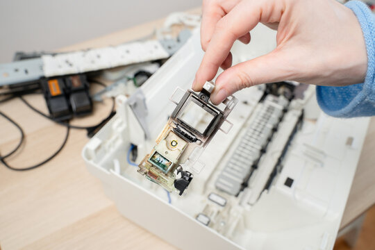 Close-up of a hand removing an inkjet printer printhead during repair and maintenance, electrical contacts and mechanical parts. Concept image for technology service, office equipment and DIY repair.
