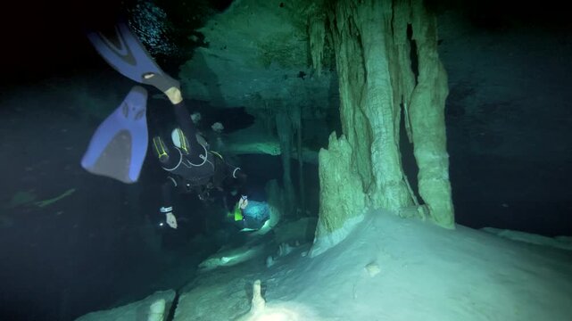 Diver with tank swims beside large calcite column inside cenote cavern in Cenote Dos Ojos, Quintana Roo, Mexico