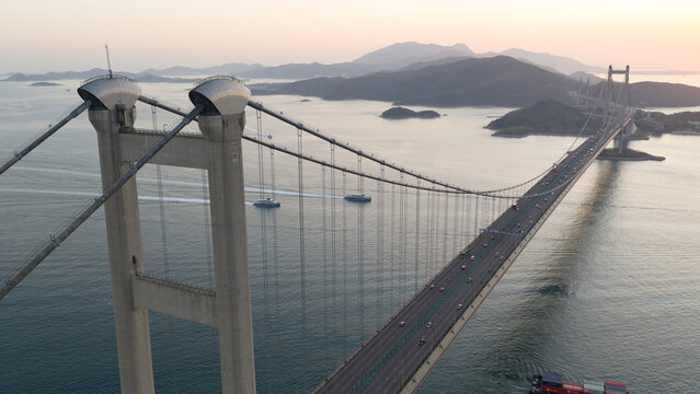 Aerial view of the Tsing Ma Bridge with traffic crossing the sea and mountains in the background during sunset Hong Kong, China.