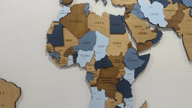 A stylized 3D wooden world map mounted on a wall, featuring different colored wood grains for various countries and continents.
