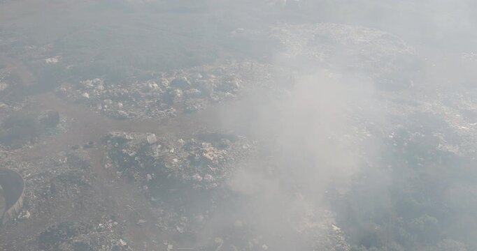Aerial panning view. Burning rubbish causing greenhouse gas, contributor to climate change.  Extreme Poverty. People living alongside dumpsite struggling to survive through waste picking.