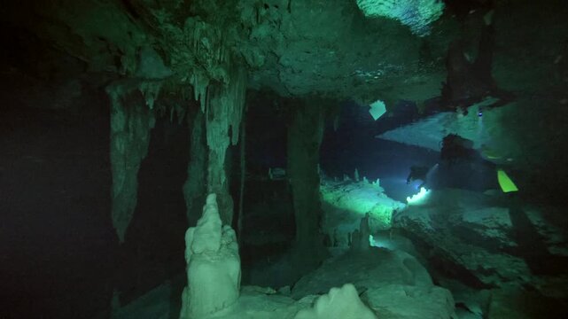 Diver moves between tall calcite columns with fins and tank in cenote cavern in Cenote Dos Ojos, Quintana Roo, Mexico