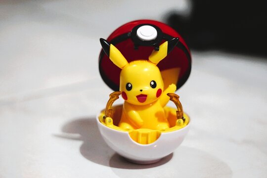 pikachu action figure emerging from an open Pok&eacute; Ball toy on a white surface
