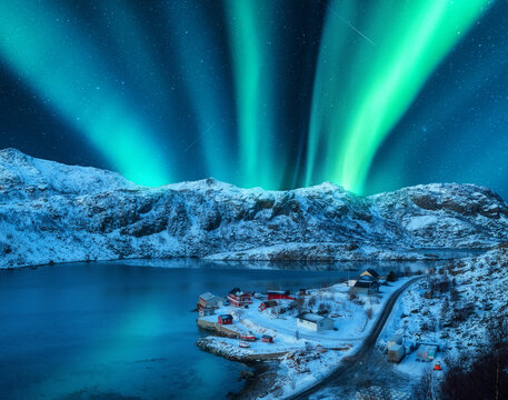 Polar lights over the snowy mountains, sea at night in Lofoten, Norway. Aerial view of aurora borealis, rocks in snow. Winter landscape with northern lights and fjord. Starry sky with aurora. Top view