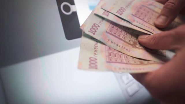 A close-up of a person's hand withdrawing money from an ATM. Ukrainian currency.