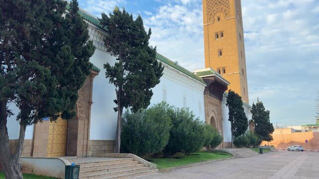 Beautiful exterior view of the Assounna mosque in Rabat. Typical moroccan architecture with white walls and minaret. Green trees and clear blue sky on the background. Historic landmarks.