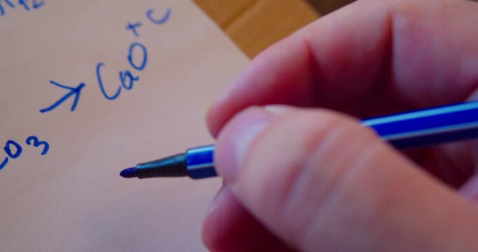 A marker writes a chemical formula on a piece of paper. Close-up. Shallow depth of field.