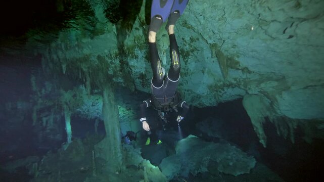 Diver swims beside massive calcite column with cave walls and floor visible in Cenote Dos Ojos, Quintana Roo, Mexico